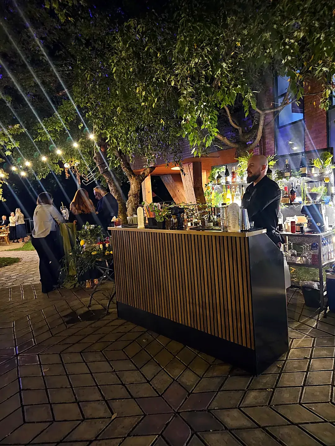 Bar mobil de cocktailuri montat seara într-o grădină, cu barman și instalații de lumini, la un eveniment privat