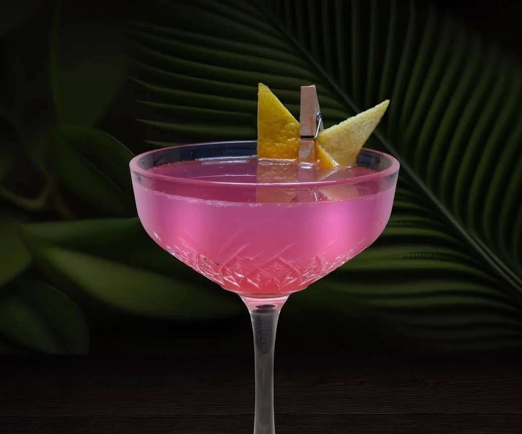 Cocktail roz servit în pahar coupe, cu coajă de lămâie, la Cofftails